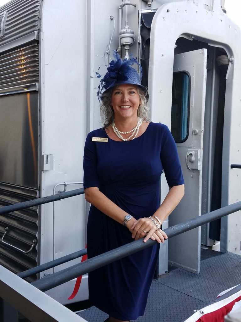 A woman in a navy dress and hat standing at the end of a silver traincar.