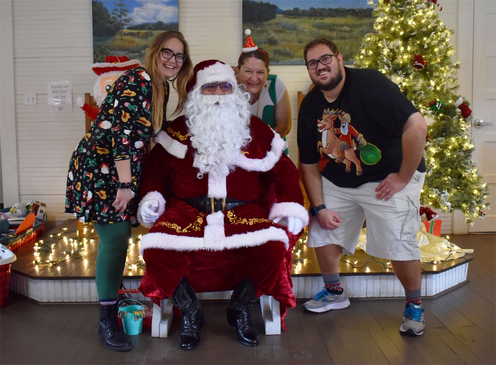 Three people posed with a Santa in cowboy boots